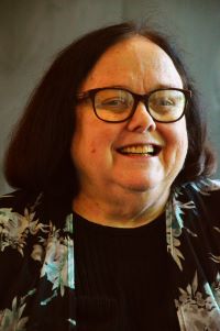 A photo of a smiling Rev. Mary Moore with dark brown hair and wearing glasses.