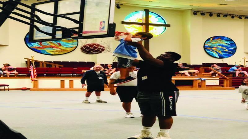 A volunteer helping a child 'dunk' at Basketball Camp.
